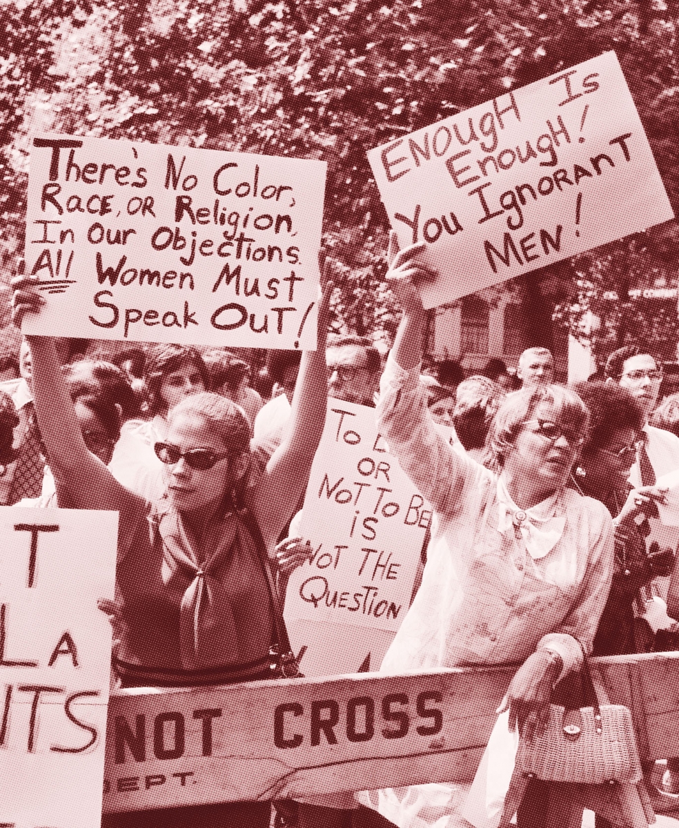 A photo of women demonstrating in New York City in the 1970s. Their handmade signs read "There's no color, race, or religion in our objections. All women must speak out!" and "Enough is enough! You ignorant men!"