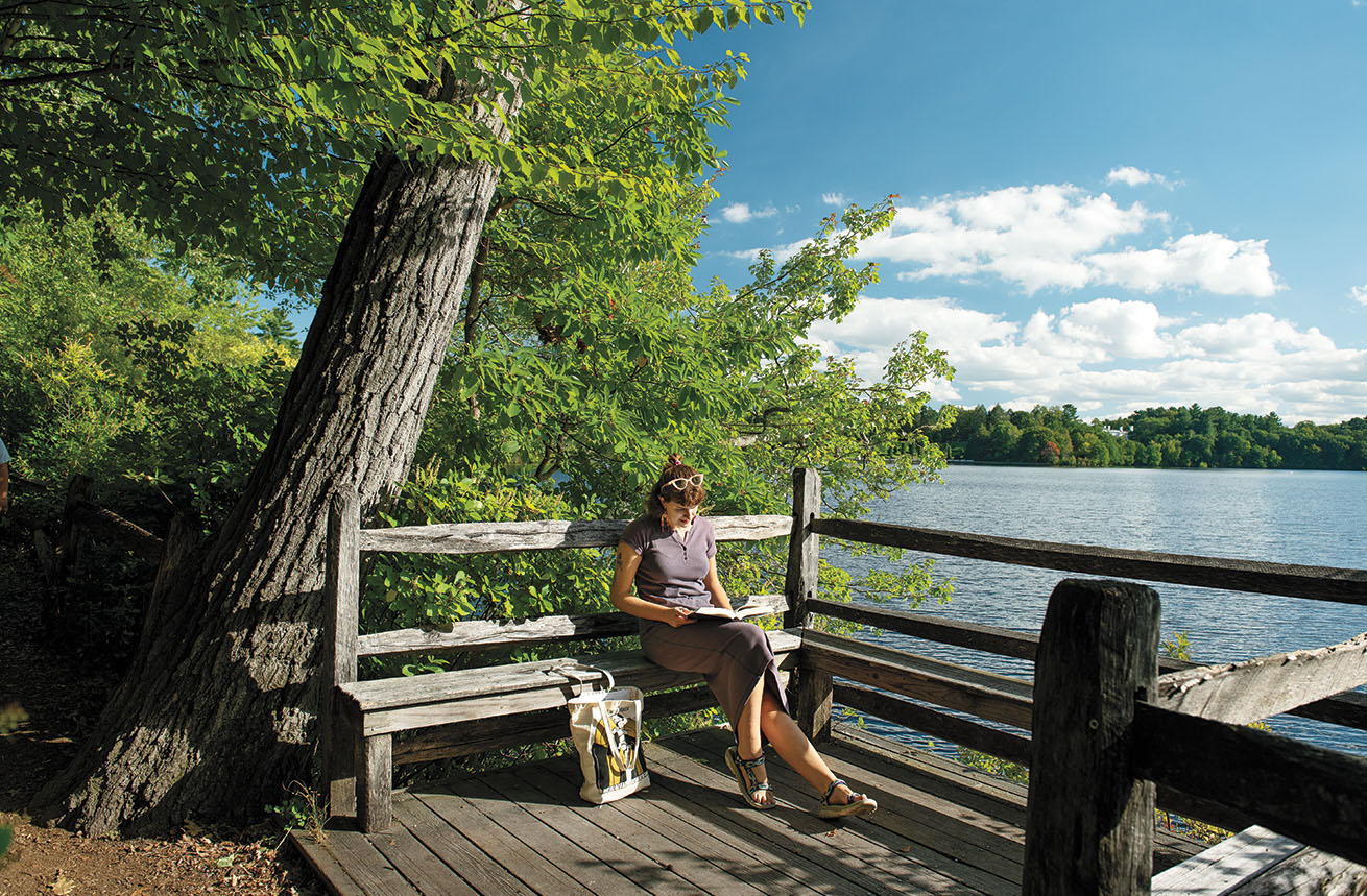 A photo shows one of the “spoonholders” along Lake Waban as Abby Martinage ’24 enjoying a break in one of the lakeside balconies envisioned by founder Henry Durant.