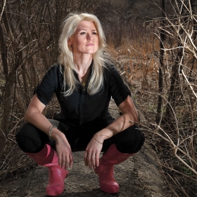 Anne Madden, wearing red rain boots, crouches in a field