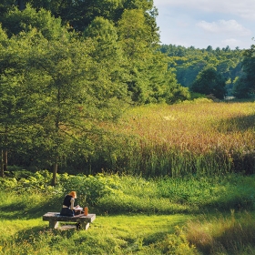 A photo shows a student sittingo n a bench in Alumnae Valley , with Lake Waban in the distance.