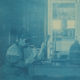 Sarah Frances Whiting examines the bones in her hand using a fluoroscope in Wellesley’s physics laboratory in 1896. A Crookes tube is on the table in front of her.