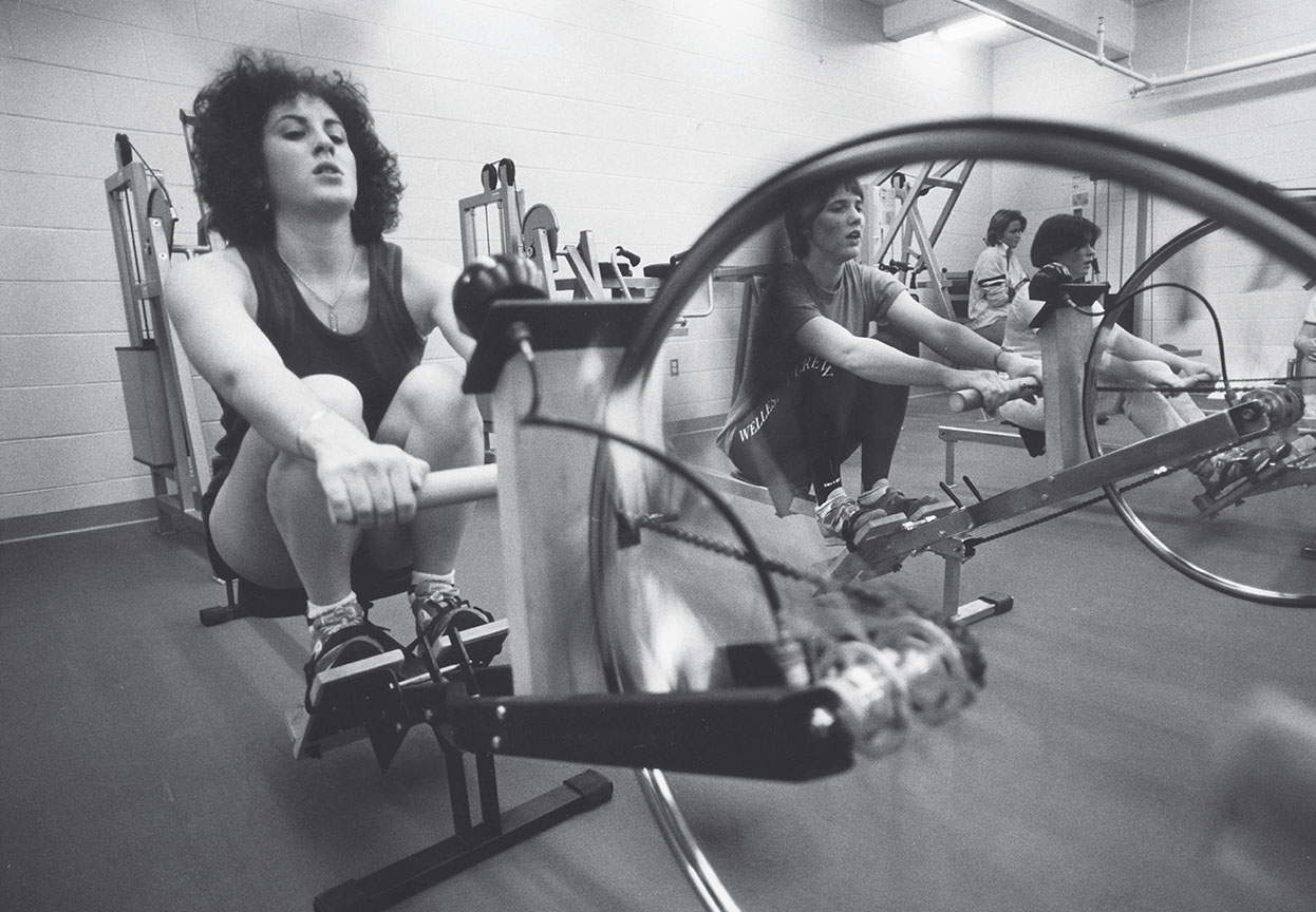 A black and white photograph of students rowing erg machines