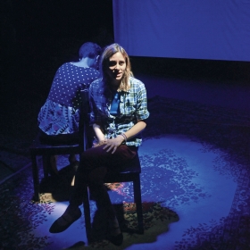 A photo taken during the production of "Decisions" shows two student actresses sitting back-to-back on a dimly lit stage.