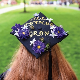 A student wears a tam decorated with flowers and the phrase "All things grow"