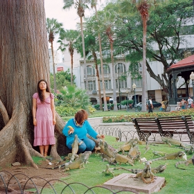 Karen Miranda Rivadeneira’s ‘Mom healing me from my fear of iguanas by taking me to the park and feeding them every weekend.' A young woman in a pink dress stands beside a large tree in a park with her eyes closed as an older woman crouching beside her feeds iguanas pieces of bananas
