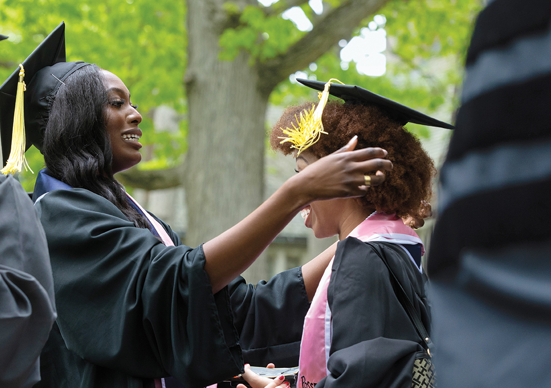 One senior adjusts another's mortarboard before the procession.