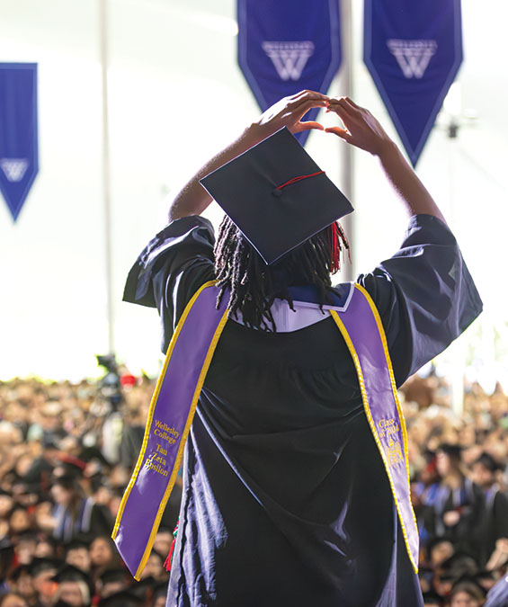 A graduate forms a heart with her hands from the Commencement stage,