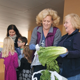 Alumnae bag heads of romaine lettuce at a community market