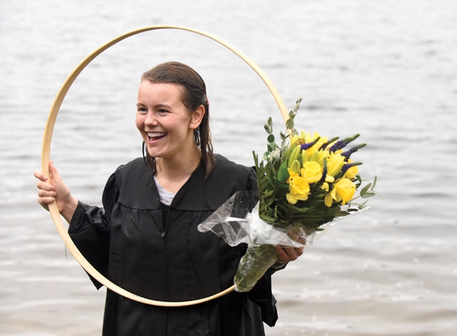  Paige Hauke ’19, the hooprolling race winner, holds her hoop and a bouquet of yellow flowers in Lake Waban.
