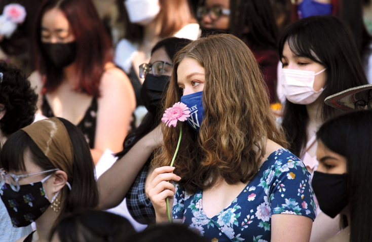 A photo shows a masked student holding a pink daisy on Flower Sunday