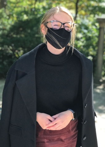A masked student models a warm coat from the Student's Aid Society Clothes Closet