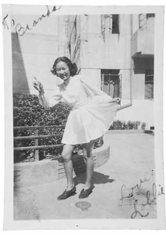 A young woman poses for the camera pointing with one hand while holding up a corner of her skirt in a kind of curtsy with the other