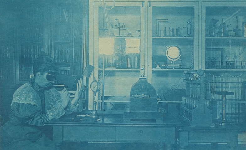 Sarah Frances Whiting examines the bones in her hand using a fluoroscope in Wellesley’s physics laboratory in 1896. A Crookes tube is on the table in front of her.