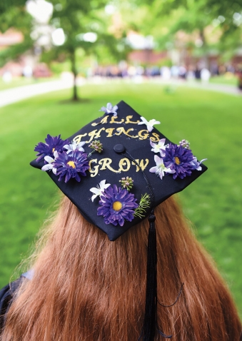 A student wears a tam decorated with flowers and the phrase "All things grow"