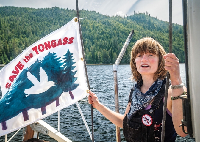 A photo of Elsa Sebastian on the deck of a boat holding a "Save the Tongass" flag