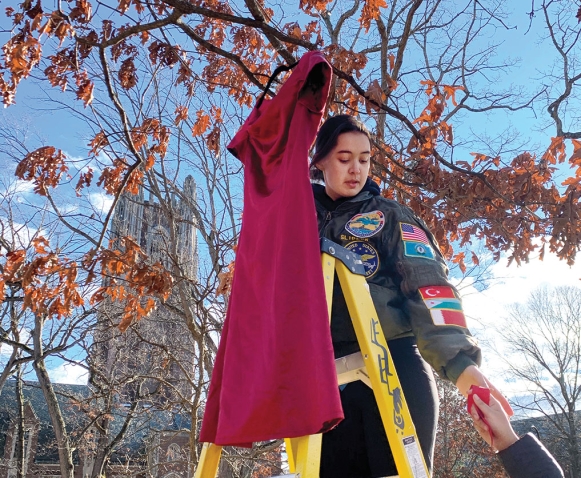 A photo shows Emma Slibeck ’24, president of NASA and a descendant of the Eastern Band of Cherokee Indians,  hanging a red dress from a tree on the Academic Quad as part of the REDress installation.