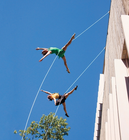 Two dancers swing from ropes attached to the new Pendleton West building