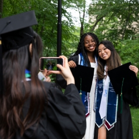 A student uses their cell phone to take a picture of two other students embracing and smiling for the camera