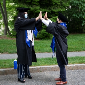 Two students in robes and tams high-five with both hands