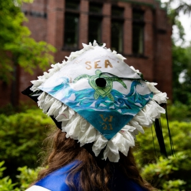 The back of a students tam decorated with the word "sea" and a painted seascape
