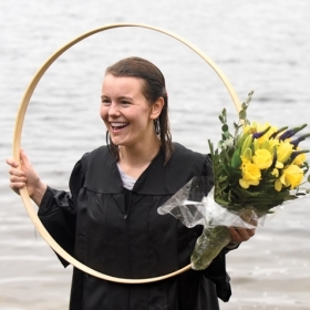  Paige Hauke ’19, the hooprolling race winner, holds her hoop and a bouquet of yellow flowers in Lake Waban.