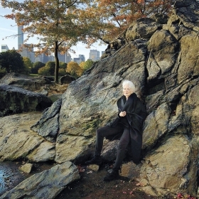 The cover of SAVING CENTRAL PARK depicts author Elizabeth Barlow Rogers leaning against a large rock outcropping in the park, with the silhouettes of skyscapers visible in the background.