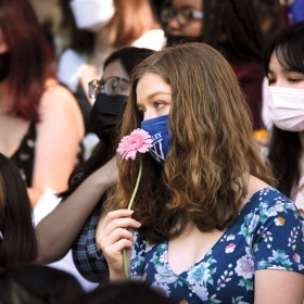 A photo shows a masked student holding a pink daisy on Flower Sunday