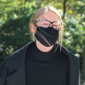 A masked student models a warm coat from the Student's Aid Society Clothes Closet