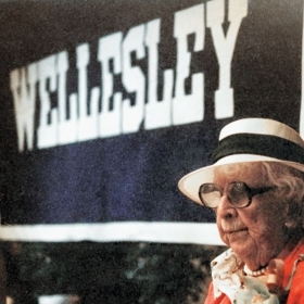 Marjorie Stoneman Douglas 2012, wearing her signature white hat, stands in front of a Wellesley banner.
