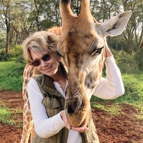 A photo shows Susan Reno Myers '74 embracing a giraffe.