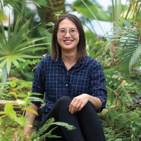 Jenn Yang '12 stands among plants in the Global Flora greenhouse.