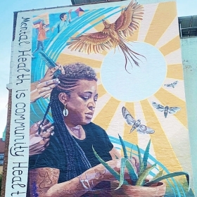 A multi-story mural on the side of a building in New York City depicts Shani Evans '96 having her hair braided.