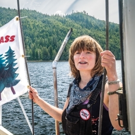 A photo of Elsa Sebastian on the deck of a boat holding a "Save the Tongass" flag