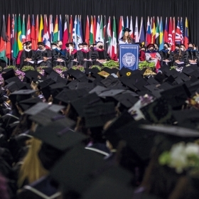 A photo shows the class of 2022 seated in the tent and looking toward the stage as Melisa Campos ’22 delivers the student speech at commencement.