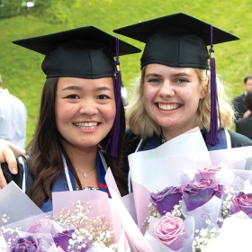 Two students holding bouquets of purple flowers