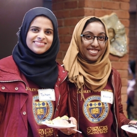 Two students wearing hijabs (head scarves) enjoy food at the Al-Muslimat 30th anniversary celebration.