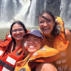 A photo of Ana Julia Daza Walter ’24 at Iguazu Falls with friends, smiling and wearing life preservers