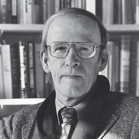 A photo portrait of poet and professor David Ferry in front of a crowded bookcase